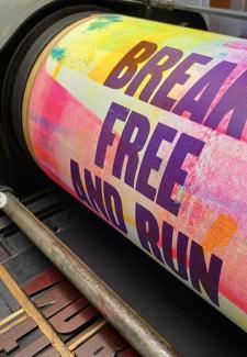 A poster with the words "Break Free and Run" is rolled on a press