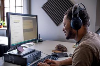 Diversity scholar intern wearing headphones works at a computer monitor in the Louie B. Nunn Center.