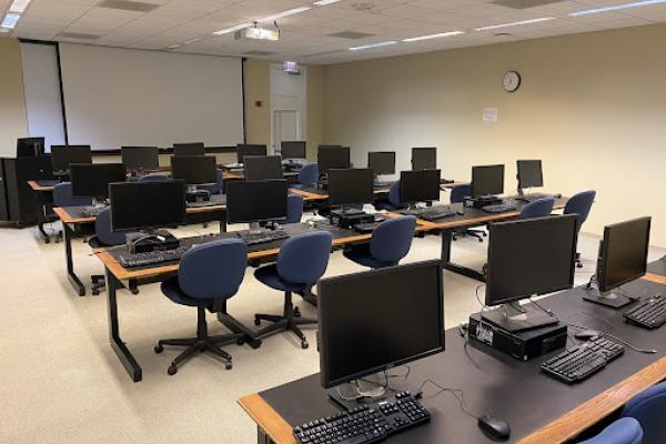 Rows of desks with computers in front of a projector screen