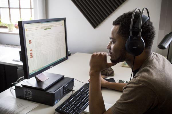 A student with headphones reads an article on his desktop computer.