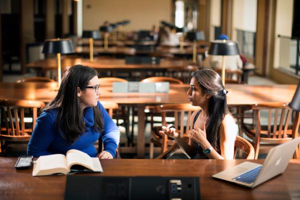 Two students in discussion at a table on the second floor of Young Library