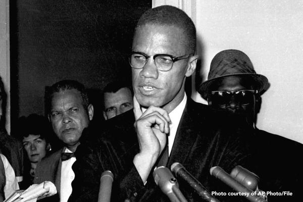 Malcom X at microphone with people standing behind him.
