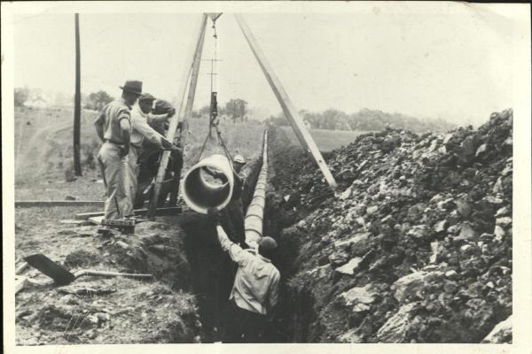 Archival photo of men laying pipe in a ditch