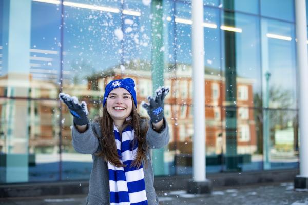 A student throws snow into the air wearing UK winter gear