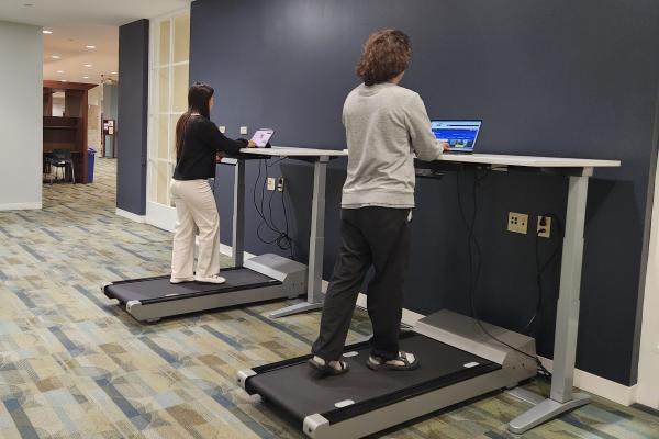 Two students work while walking on treadmill desks