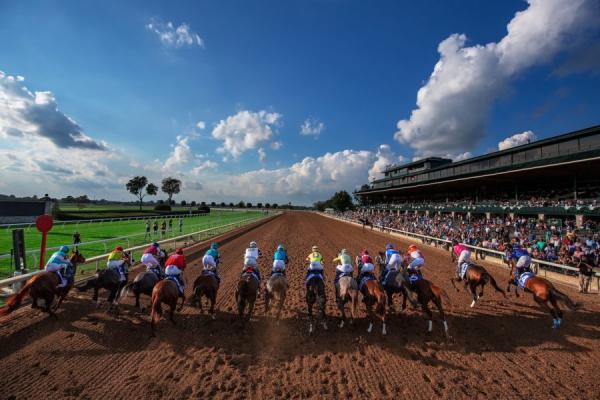 Horses race down dirt track of Keeneland beneath clouds