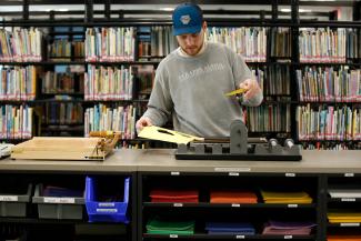 A man operates a CriCut machine in front of bookcases