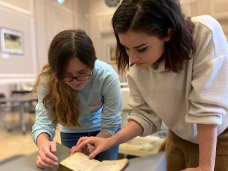 Two female students look at a rare book in the Great Hall.