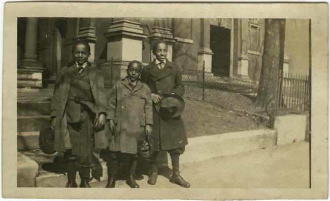 Three unidentified boys stand in front of steps with winter coats and hats